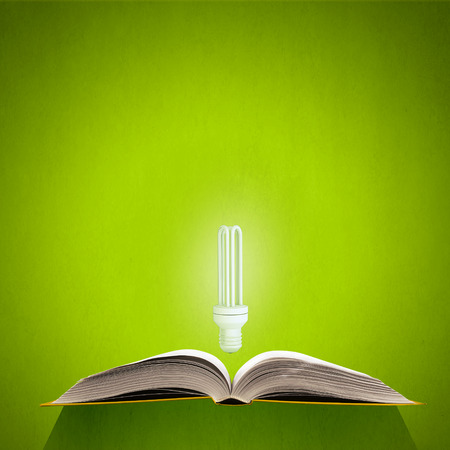 Old opened book and glowing light bulbの写真素材