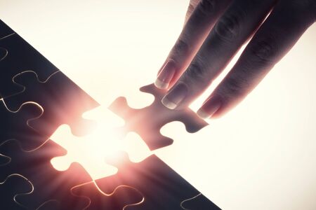Close up of hands connecting puzzle element and making jigsaw completeの写真素材