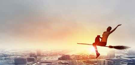 Happy young woman flying in sky on broomの写真素材