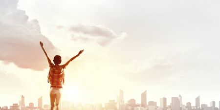 Rear view of girl with hands up facing sunrise abone cityの写真素材
