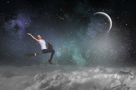 Happy young woman flying in sky on broomの写真素材