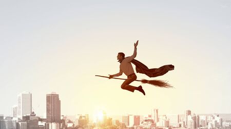 Young businessman flying on broom high in skyの写真素材