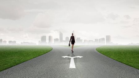 Back view of businesswoman standing on crossroads and making choiceの写真素材