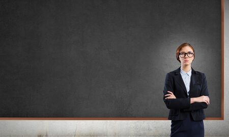 Young confident woman wearing glasses standing near blank blackboardの写真素材