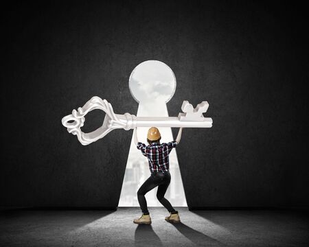 Young engineer woman lifting big key above headの写真素材