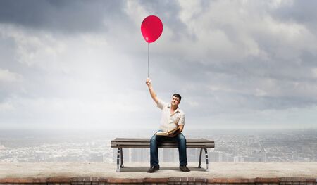 Fat man sitting on bench with book and balloon in handの写真素材