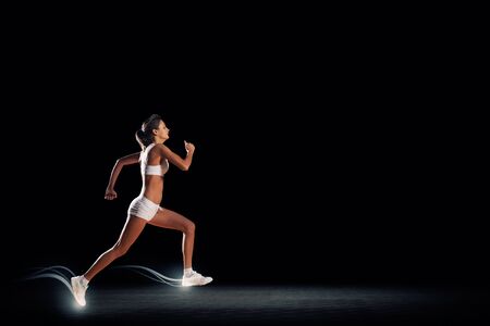 Young woman athlete running fast on dark backgroundの写真素材
