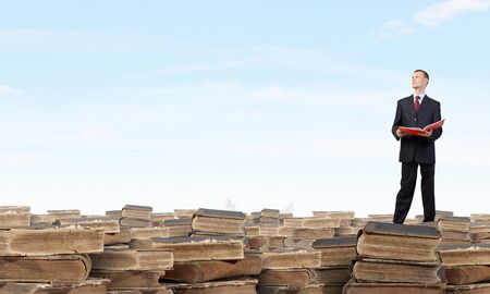 Young businesman standing on pile of old booksの写真素材