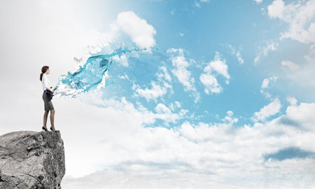 Cheerful businesswoman standing on rock edge and playing electric guitarの写真素材