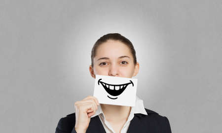 Pretty young girl holding white card with drawn smile with teethの写真素材