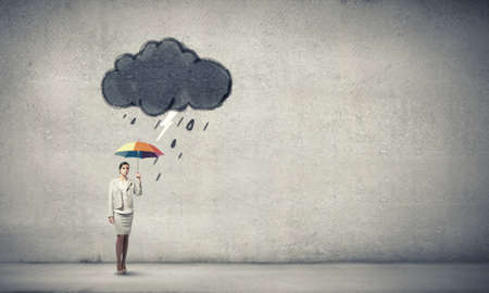 Young businesswoman with colorful umbrella under black cloudの写真素材