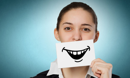 Pretty young girl holding white card with drawn smile with teethの写真素材