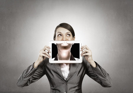 Beautiful young woman holding tablet pc against her mouthの写真素材