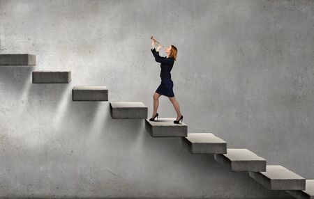 Young businesswoman on staircase proclaiming something in hornの写真素材