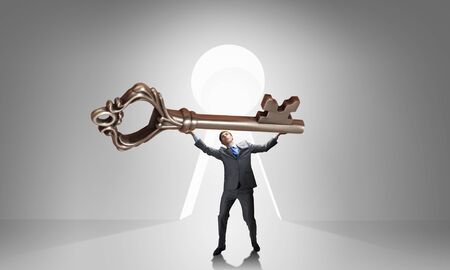 Young businessman and lifting big key above headの写真素材