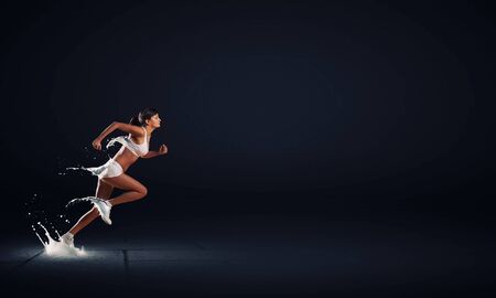 Young woman athlete running fast on dark backgroundの写真素材