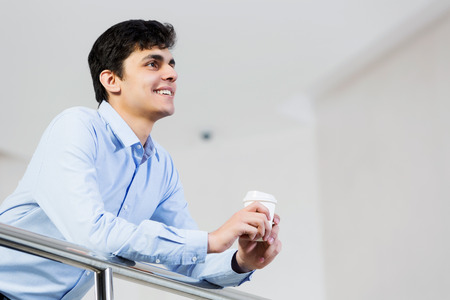 Young man standing at balcony with plastic cup in handsの写真素材