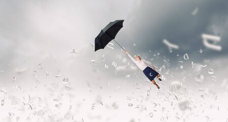 Young businesswoman flying high in sky on black umbrellaの写真素材
