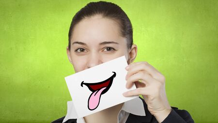 Pretty young girl holding white card with drawn smile showing tongueの写真素材