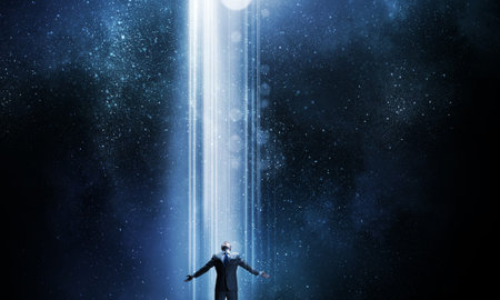 Businessman with hands spread apart standing in light coming from above