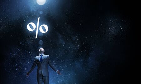 Businessman with hands spread apart standing in light and percent sign aboveの写真素材