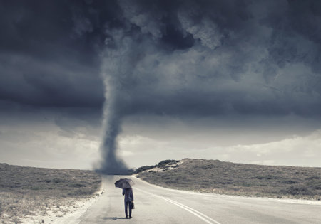 Back view of businessman with umbrella and suitcase facing tornado
