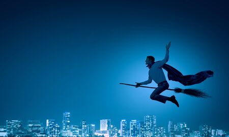 Young businessman flying on broom high in skyの写真素材