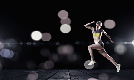 Young woman athlete running fast on dark の写真素材