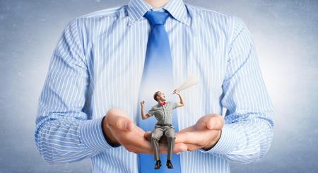 Young businessman sitting in palms and screaming emotionally in paper trumpetの写真素材