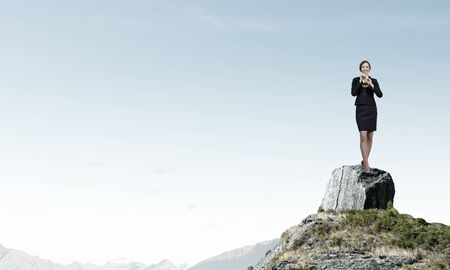 Cheerful businesswoman standing on rock top and playing fifeの写真素材