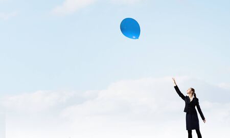 Young businesswoman reaching hand to touch balloon in skyの写真素材