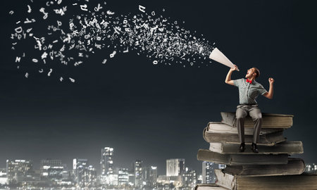 Young man in bow tie screaming in paper trumpetの写真素材