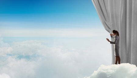 Young businesswoman opening stage curtain to another realityの写真素材