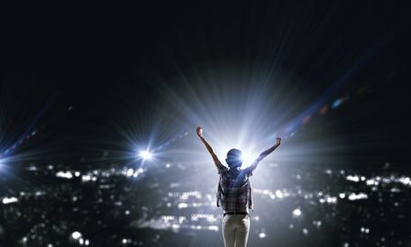 Rear view of young woman with hands up looking at night cityの写真素材