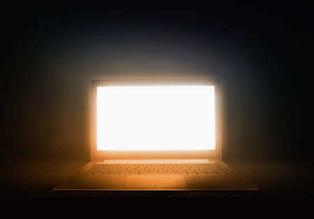 Open laptop with light coming from screen on dark backgroundの写真素材