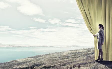 Young businesswoman opening stage curtain to another realityの写真素材