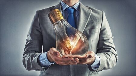 Young businessman presenting glass glowing light bulb in his handsの写真素材