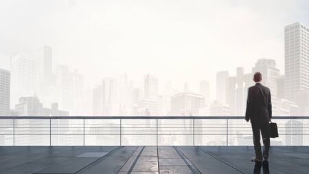 Back view of businessman standing on roof looking at cityの写真素材