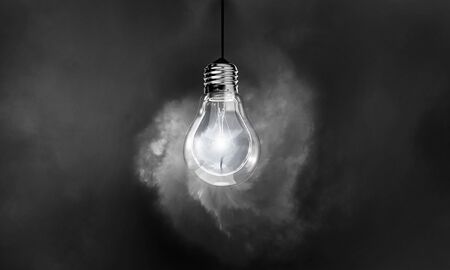 Glowing light bulb on dark background hanging from aboveの写真素材