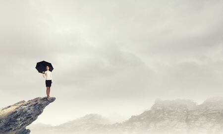 Young businesswoman with black umbrella standing on topの写真素材