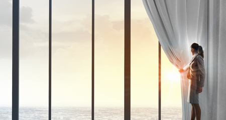 Businesswoman pulling curtain and cityscape behind itの写真素材