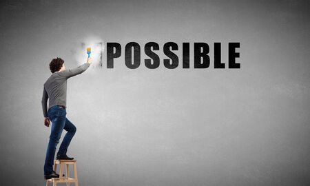 Man changing word impossible in to possible by erasing part of word with paint brushの写真素材