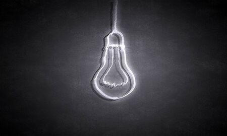 Glowing light bulb on dark background hanging from aboveの写真素材