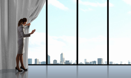 Businesswoman pulling curtain and cityscape behind itの写真素材