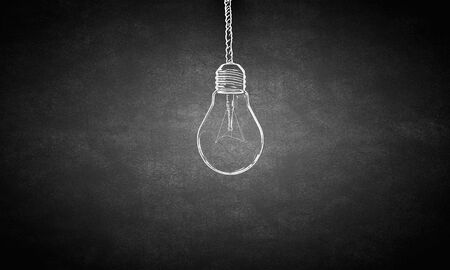 Glowing light bulb on dark background hanging from aboveの写真素材