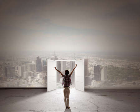 Rear view of woman with hands up entering opened doorの写真素材