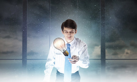 Young businessman examining glass glowing light bulbの写真素材