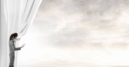 Young businesswoman opening stage curtain to another realityの写真素材