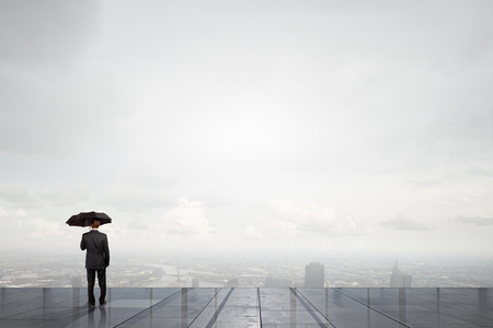 Back view of businessman with umbrella looking at cityの写真素材