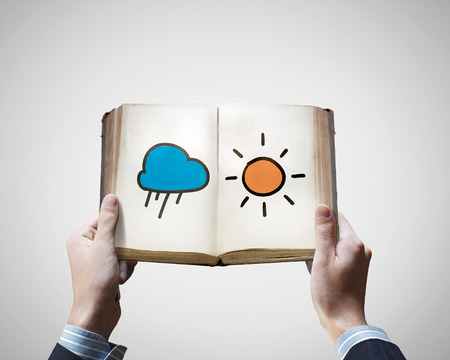 Close up of male hands holding old book with sun a cloud illustrationの写真素材